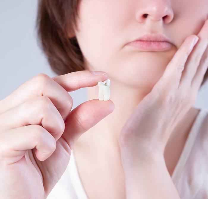 Nose-to-chest view of woman frowning holding hand to face and an extracted tooth